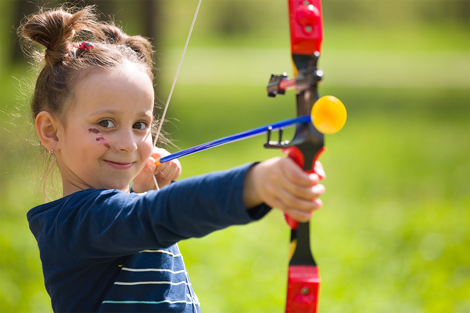 Little girl facing camera holding a soft archery bow. 