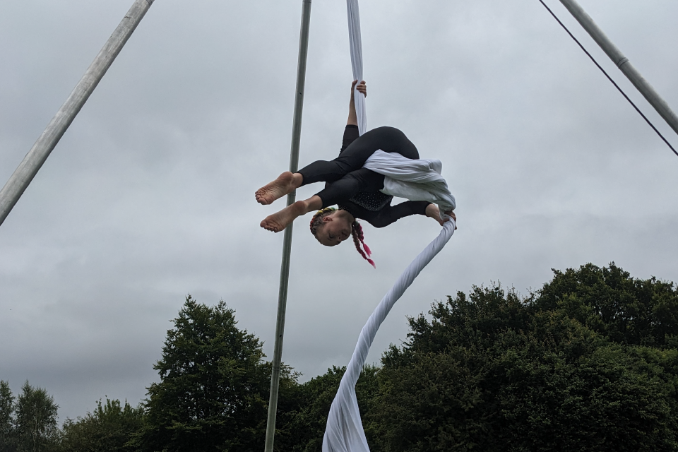 Photograph of a young girl practiving aerial silks outdoors. 
