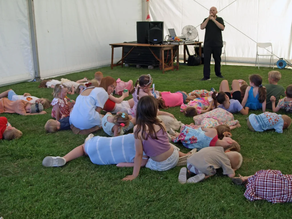 Children lying on the grass inside a marquee at the Parbold Village Show Friday Night Disco 2025, listening to a live entertainer.