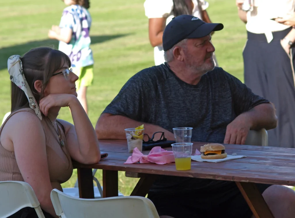 Man and woman relaxing at a wooden picnic table with drinks and a burger at the Parbold Village Show Friday Night Disco 2025.