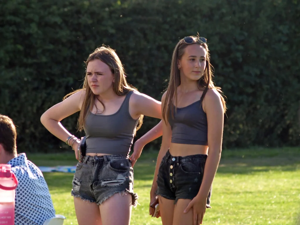 Two teenage girls standing in the sun watching the entertainment at the Parbold Village Show Friday Night Disco 2025.