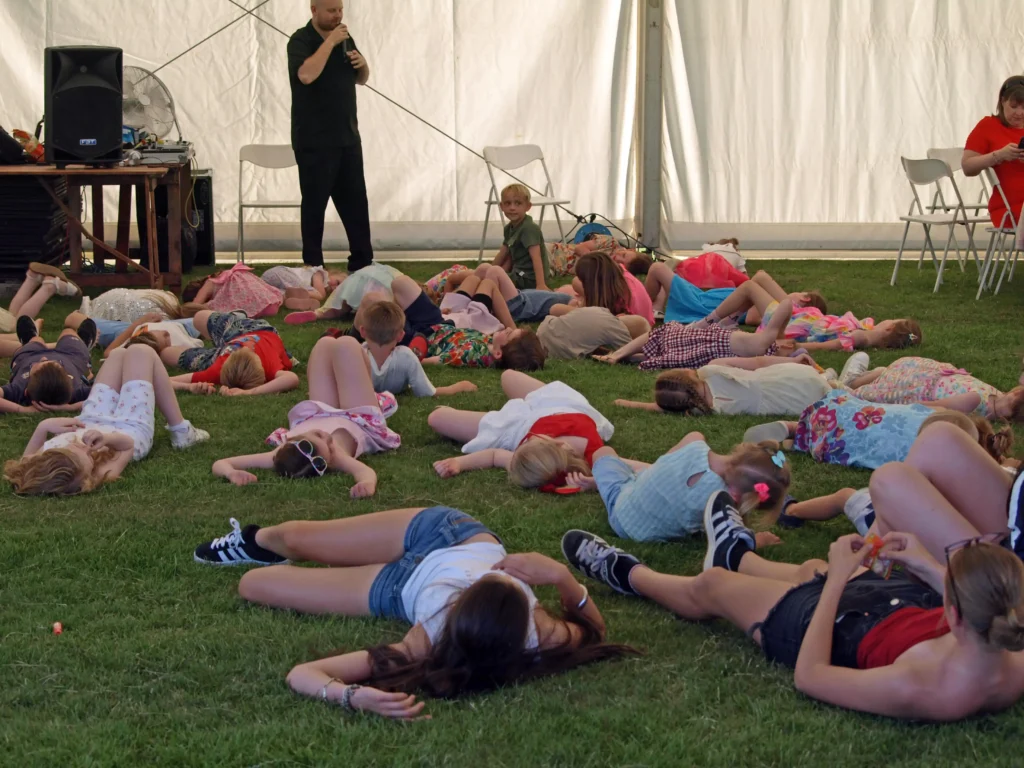 Children lying on the grass during a fun interactive activity inside the marquee at the Parbold Village Show Friday Night Disco 2025.
