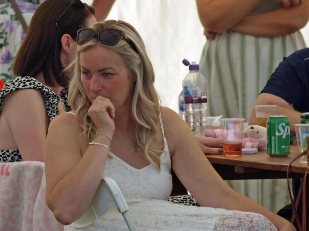 Woman in a white lace dress sitting inside the marquee at the Parbold Village Show Friday Night Disco 2025, surrounded by drinks and friends.
