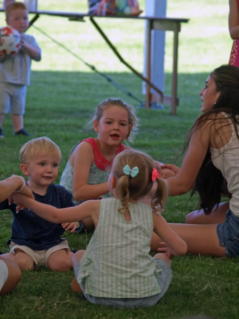 Smiling children holding hands in a circle game at the Parbold Village Show Friday Night Disco 2025, with a toddler holding a football in the background.