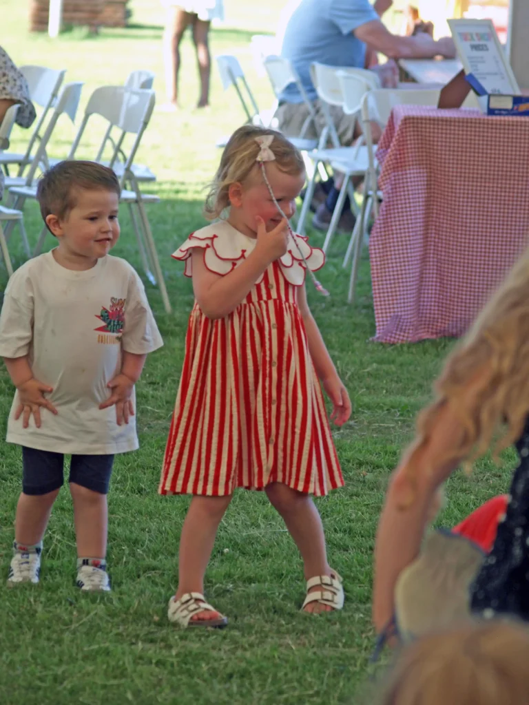 Two toddlers watching the entertainment at the Parbold Village Show Friday Night Disco 2025, one wearing a red and white striped dress.
