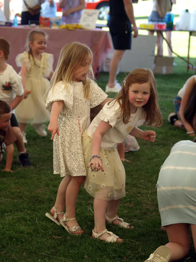 Two young girls balancing and laughing during a party game at the Parbold Village Show Friday Night Disco 2025.