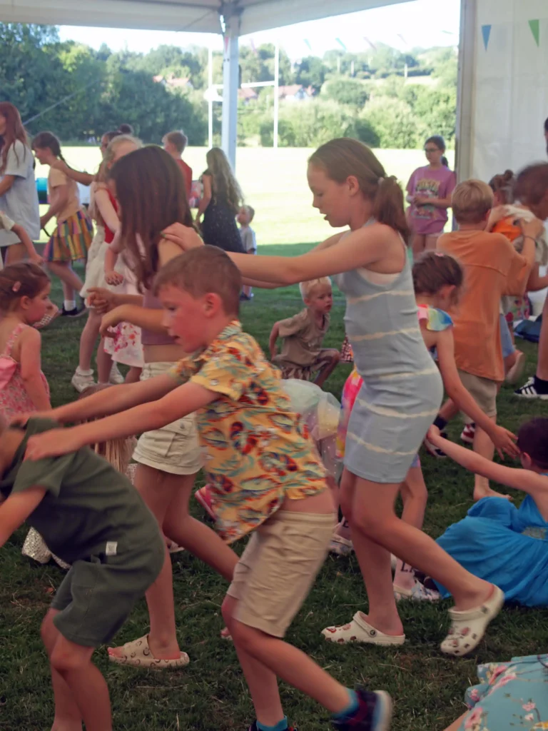 Children moving together in a conga line during the Parbold Village Show Friday Night Disco 2025, with the marquee and countryside in the background.