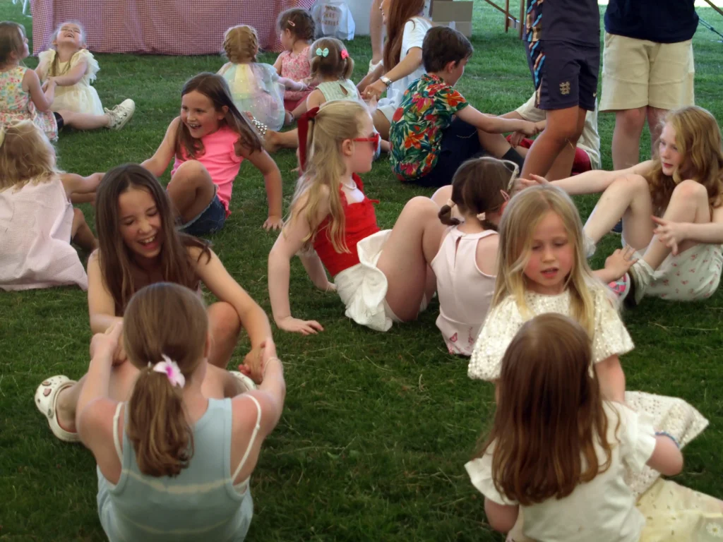 Groups of children laughing and working together in a partnered sitting game on the grass at the Parbold Village Show Friday Night Disco 2025.