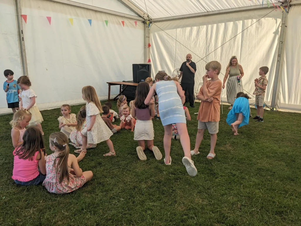 Children playing an energetic game on the grass under the marquee at the Parbold Village Show Friday Night Disco 2025, led by an entertainer.