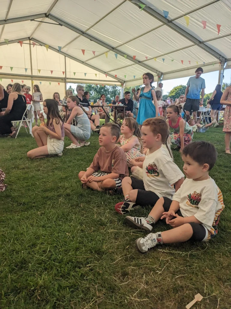 Children sitting on the grass watching the entertainment under the marquee at the Parbold Village Show Friday Night Disco 2025.